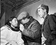 Dr. Walter Crewson, Hamilton eye specialist, examines eyes of Eskimo woman in corner of one of the NASCOPIE's holds 1947