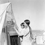 Inuit woman and child looking at Family Allowance poster in Baker Lake. [The woman has been identified as Winnie Attungala.] 1948.