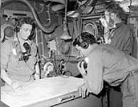 Three army men inside a ship looking at a map ca. 1951