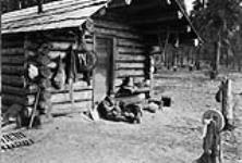 Man sitting outside log cabin with his dog n.d.