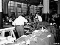Des hommes pressant des uniformes de l'Armée canadienne au département dupressage d'une grande entreprise textile déc. 1939