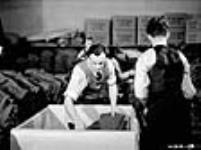 Des hommes trient et emballent des uniformes de l'Armée canadienne terminés dans une grande usine de vêtements en vue de leur expédition au quartier-général de l'armée déc. 1939