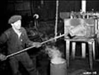 Balles de fusil-mitrailleur Bren. Un moulage de balles rougeoyant est sorti d'un four par un ouvrier métallurgiste immédiatement avant d'être placé sous un marteau pilon pour façonnage. L'ouvrier utilise une longue barre de fer en raison de la chaleur intense Dec. 1939