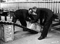 Des ouvriers chargent des caisses d'expédition remplies de balles de fusil-mitrailleurs Bren sur une rampe à l'usine de munitions de la National Steel Car Corporation Ltd Dec. 1939