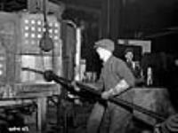 Un ouvrier place des moules de pièces de fusil-mitrailleur Bren à chauffer dans un four de fonderie Dec. 1939