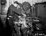 Des ouvriers utilisant un tour d'atelier dans une usine de munitions canadienne. Le liquide blanc est versé en permanence pour prévenir la surchauffe du métal Dec. 1939
