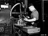 Des ouvriers utilisant un tour d'atelier dans une usine de munitions canadienne. Le liquide blanc est versé en permanence pour prévenir la surchauffe du métal Dec. 1939