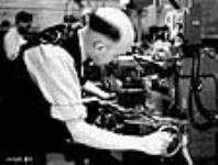 Dans une fabrique canadienne, un employé utilise une machine pour façonner des lames-chargeurs de fusils-mitrailleurs Bren Dec. 1939