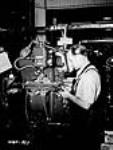 Workman operates lathe to machine small parts of Bren gun or shells July 1940