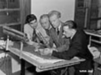 Des hommes à une table de travail avec des plans, examinant une douille au cours du processus de fabrication des calibres Oct. 1940