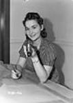 Une femme, à une table de travail avec un plan, examinant du matériel au cours du processus de fabrication des calibres Oct. 1940