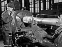 Un ouvrier mange un sandwich pendant l'usinage d'un canon sur un tour à l'aciérie Sorel Steel Dec. 1940