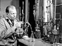 Un chimiste dans un laboratoire de l'aciérie de la Sorel Steel Co. retiredu liquide d'un bocal rond à fond plat pour déterminer les composants des échantillons d'acier provenant de la fonderie Dec. 1940