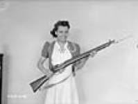 Une femme pose avec une baïonnette de fusil finie dans une usine d'armes légères à Long Branch juil. 1941