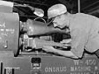 Workman positions wooden butt-end of a rifle in a lathe in a small arms plant, Long Branch juil. 1941