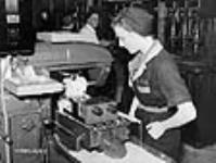 Woman machinist observes lathe working on a rifle part in a small arms plant, Long Branch juil. 1941