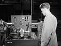 Un ouvrier surveille une machine Magnaflux qui détecte par magnétisme les imperfections dans les métaux à la Canadian Propeller Co Mar. 1942