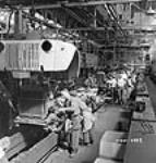 Des ouvriers descendent l'ensemble ailes et calandre sur le châssis d'un camion sur la chaîne de montage finale à l'usine de la compagnie Ford du Canada 2 July 1942