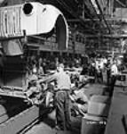 Des ouvriers descendent l'ensemble ailes et calandre sur le châssis d'un camion sur la chaîne de montage finale à l'usine de la compagnie Ford du Canada 2 July 1942