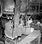 Un ouvrier portant un casque de sécurité guide un pistolet à air compriméqui compacte le sable dans des moules dans la fonderie de la compagnie Ford du Canada 2 July 1942