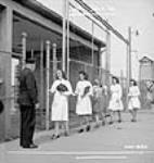 Female munitions workers present identification to the Dominion Arsenals Ltd. plant guard as they arrive 24 Aug. 1942