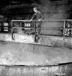 L'aide-électricien Edouard-Charles Gravel regarde attentivement dans un des précipitateurs de l'atelier d'alumine de l'usine Alcan Aluminium Limitée d'Arvida Jan. 1943