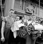 Les membres du nouvel équipage portent dans les bras leur literie après avoir embarqué sur un nouveau navire de charge lors de son essai de fonctionnement et avant qu'il ne parte vers un autre port July 1943