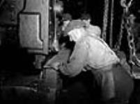 Pendant la construction d'un navire, des ouvriers guident des plaques d'acier sur une machine qui les coupe sept. 1943