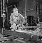 Un ouvrier portant un masque de protection transparent conduit une machine et lime les pièces d'une locomotive X-Dominion pour expédition en Inde nov. 1943