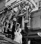 Dans une fabrique de munitions, des ouvrières manipulent des douilles pendant que des hauts-parleurs diffusent de la musique Nov. 1943