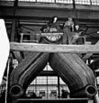 Workmen in the Canadian Vickers shipyard, Jean Rivet (emerging from the boiler) bucks rivets for Joe Hurd during construction of a Frigate in the Canadian Vickers yard sept. 1943