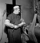 L'ouvrier F.N. Herald utilise une ponceuse à disque électrique sur une enveloppe de torpille avant de la peindre à l'usine John Inglis Co May 1944
