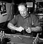 Workman Richard Chowns of Humber Bay, Ont. works burring and cleaning Sten breech blocks for inspection at the Small Arms Ltd. plant avril 1944