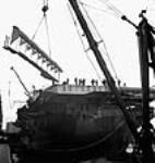 View of the derrick scow swinging the cut off flight deck round down during the construction of Aircraft Carrier Escort vessels in the Burrard Dry Docks mai 1944
