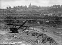 Vue de la plus grande pelle mécanique canadienne chargeant un train de minerai d'amiante dans une mine à ciel ouvert, la mine Jeffrey, exploitée par la société Johns-Mainville Canada Inc June 1944