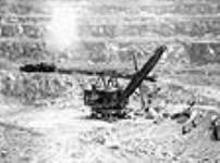 Vue d'une pelle mécanique chargeant un train de minerai d'amiante dans une mine à ciel ouvert, la mine Jeffrey, exploitée par la société Johns-Mainville Canada Inc June 1944