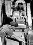 L'ouvrier Bratien Nourry conduit une presse à bardeaux pour découper dansdes panneaux d'amiante rigides des bardeaux à imitation de bois à l'usine Johns-Mainville Canada Inc juin 1944