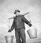 "Chore-man" Andres Budge of Maniwaki, Quebec, carrying water in buckets by means of a yoke across his shoulders at M. Kearney's logging camp mars 1943