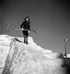 Un garçon avec un bâton de hockey descend en patins sur un dépôt provisoire de billes recouvert de glace au lac Sloe Mar. 1943
