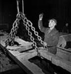 Workman directs the hoisting of an X-Dominion locomotive part in a factory Winter 1943