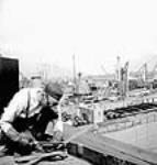 Un soudeur soude une pièce au premier plan d'une vue générale de navires marchands de la Victoire au chantier naval de Burrard mai 1943