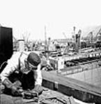 Un soudeur soude une pièce au premier plan d'une vue générale de navires marchands de la Victoire au chantier naval de Burrard mai 1943