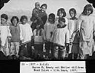 Nurse G. Keary with Inuit children outside in the Pond Inlet, Nunavut area [From left to right: Eunice Koonoo Arreak, Elisapee Muckpah, Rita Paniloo Nashook, Joseph Koonoo being held by Nurse Keary, Rebecca Qitsualik (in front of the nurse), Koonoo Killiktee, Enooya Enook, Aasarmi Kippomee (boy standing in front of Enooya Enook), Arnaujumajuq Piungittuq Qillaq (girl second from the far right), and Leah Merkosak (partially cut off on far right)] Sept. 11, 1937.