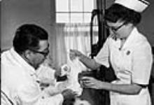 Nurse is assisting doctor with putting a cast on a patient at the Frobisher Bay Hospital 1959