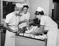 Two nurses in training are watching a nurse handle a newborn baby in the maternity ward at the Nightingale School of Nursing in Toronto, Ont c 1960
