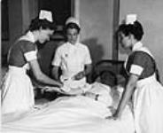 A nurse is observing as a nurse in training tends to a patient's arm at the School of Nursing at Sherbrooke Hospital c 1950