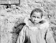 [Portrait of an unidentified Inuit child wearing a parka in front of a mound of dirt and grass, possibly Nunavut]. Original title : Half breed eskimo children (Portugese), [Nunavut?] n.d.