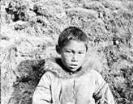 [Portrait of an unidentified child wearing a parka in front of a mound of dirt and grass, possibly Nunavut]. Original title : Half breed eskimo children (Kanaka), [Nunavut?] n.d.