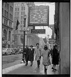 People walking down a Toronto sidewalk, a sign for an evangelical book shop and a tavern side-by-side January 19, 1946