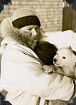 Dr. "Perce" Corbett, station doctor at Chesterfield Inlet, holding an orphaned polar bear cub 1952